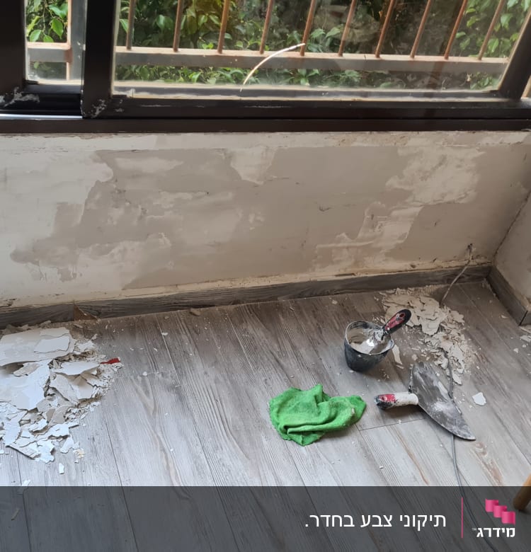 קיר מתוקן עם שפכטל, מברשת ובד ירוק על הרצפה